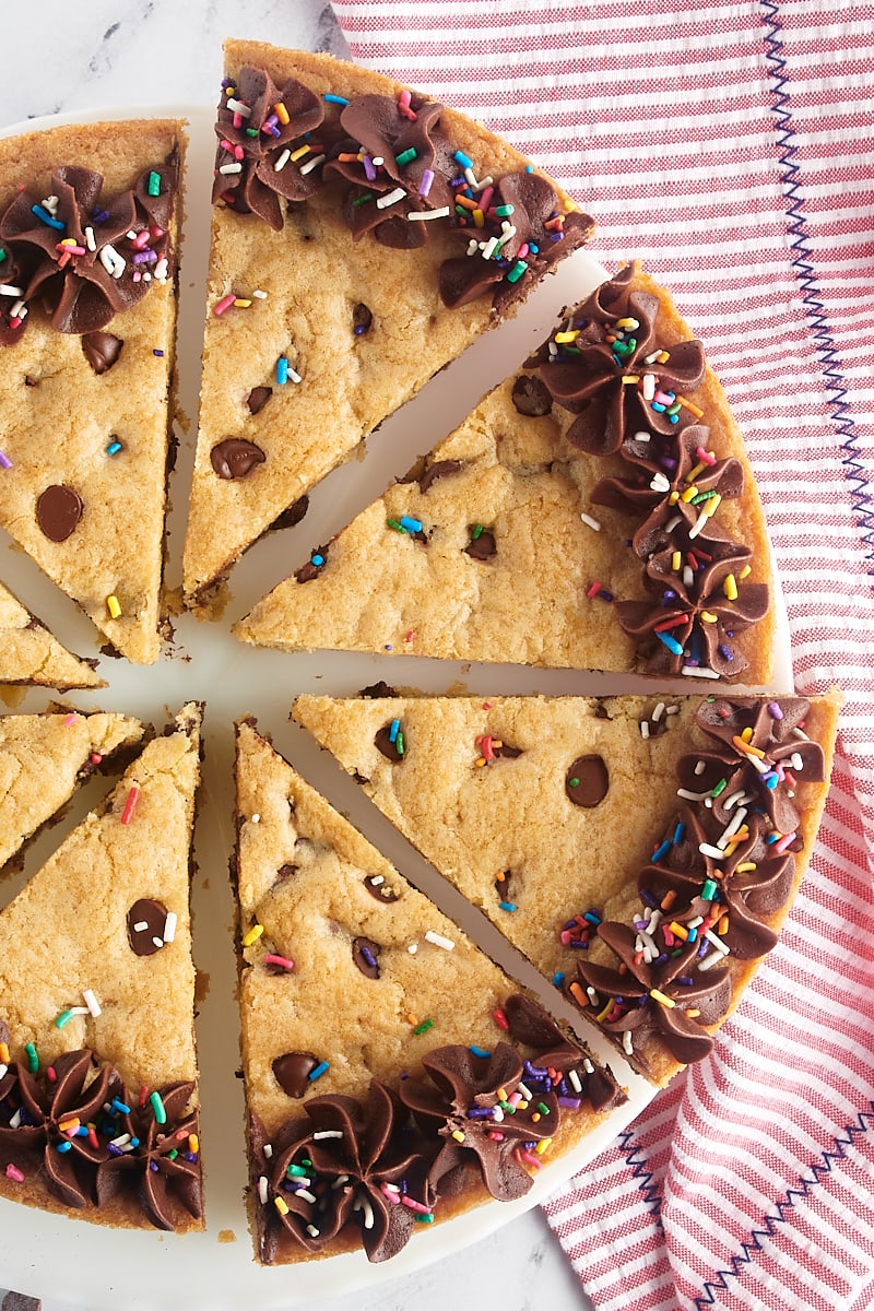 overhead view of sliced chocolate chip cookie cake on a white cake stand