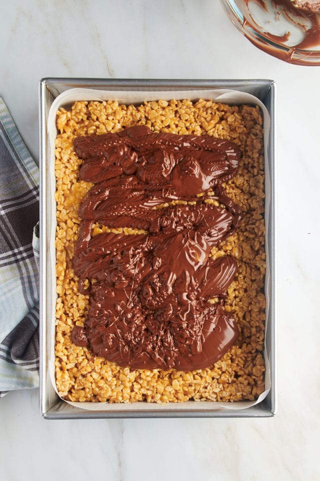 Overhead view of melted chocolate and butterscotch added to rice crispy layer in pan