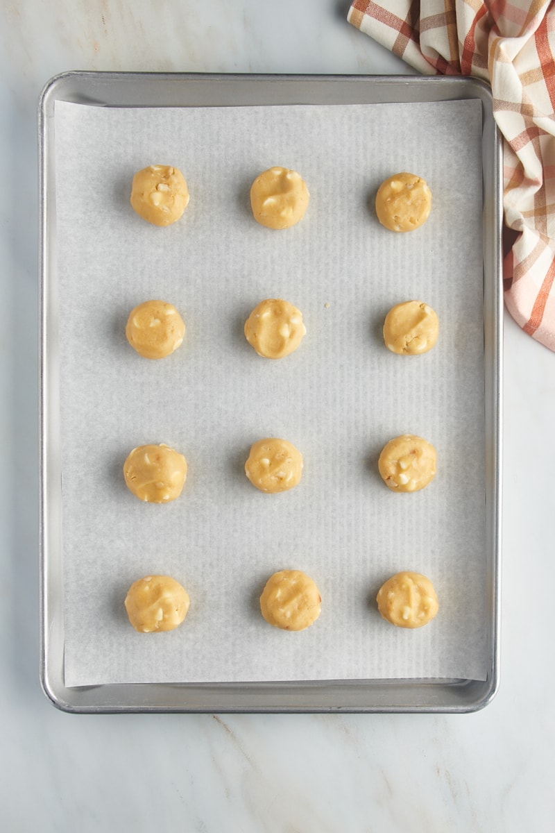 Overhead view of white chocolate macadamia nut cookie dough on a baking sheet.