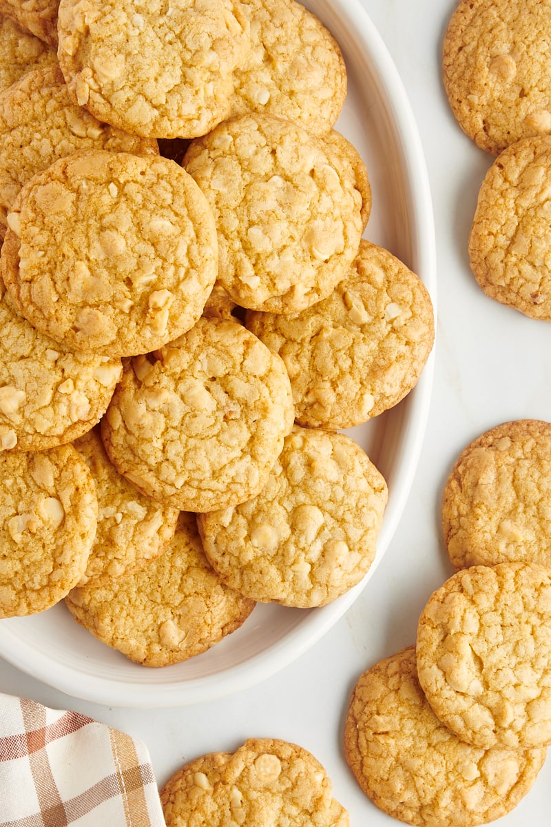 Overhead view of white chocolate macadamia nut cookies on a platter and on the countertop.