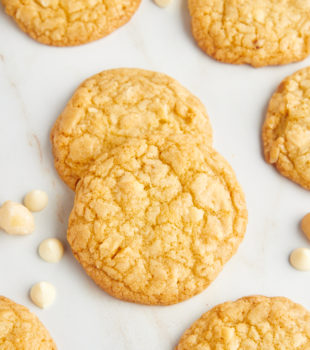 Overhead view of white chocolate macadamia nut cookies with white chocolate chips and macadamia nuts scattered in background
