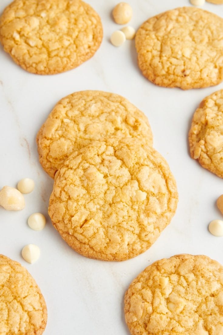 Overhead view of white chocolate macadamia nut cookies with white chocolate chips and macadamia nuts scattered in background