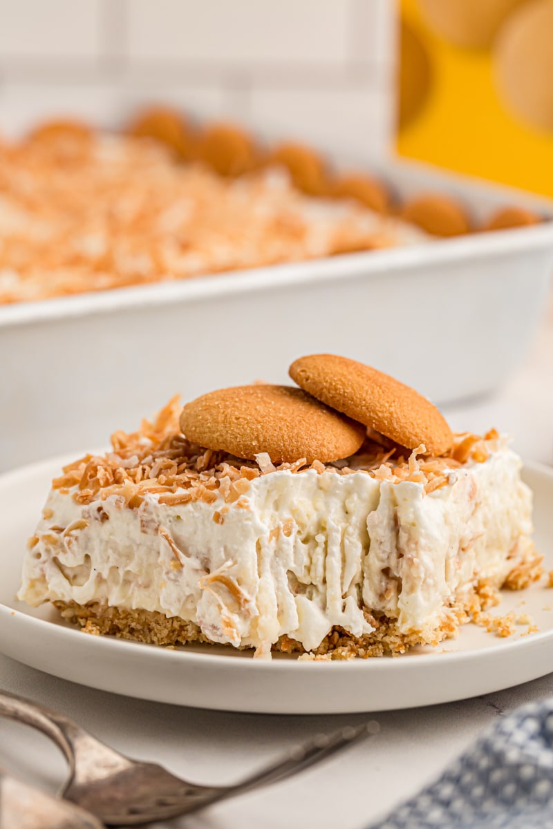 Coconut cream pie bar on plate with corner eaten and two vanilla wafers set on top