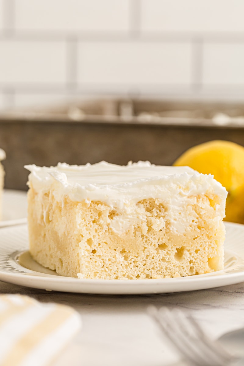 Side view of lemon poke cake slice on plate, showing light texture and filling