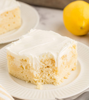 Piece of lemon poke cake on white plate, with corner eaten