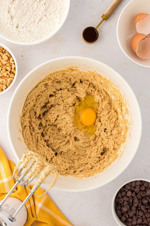 overhead view of an egg added to creamed butter and brown sugar in a white mixing bowl