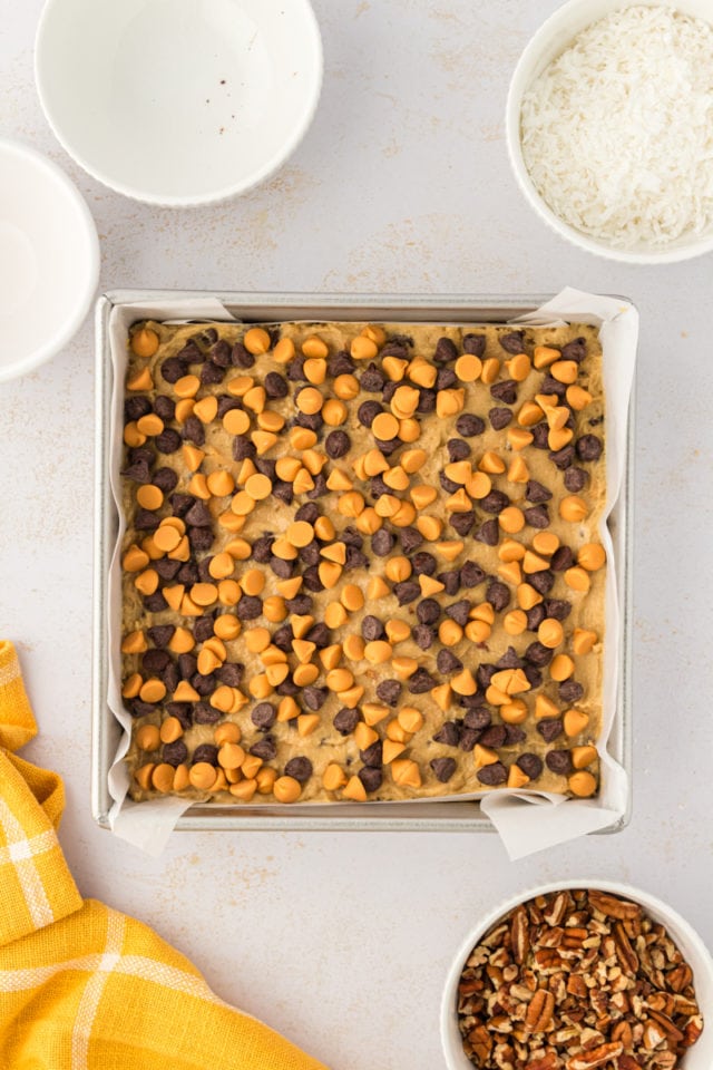 overhead view of chocolate chips and butterscotch chips scattered over toffee squares dough in a baking pan