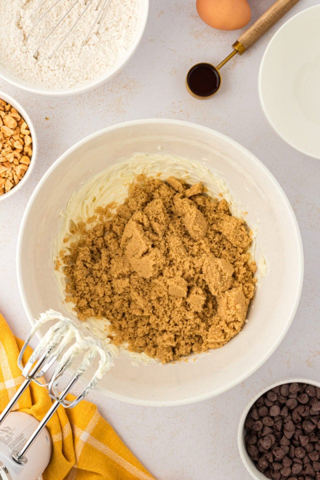 overhead view of brown sugar added to creamed butter in a white mixing bowl
