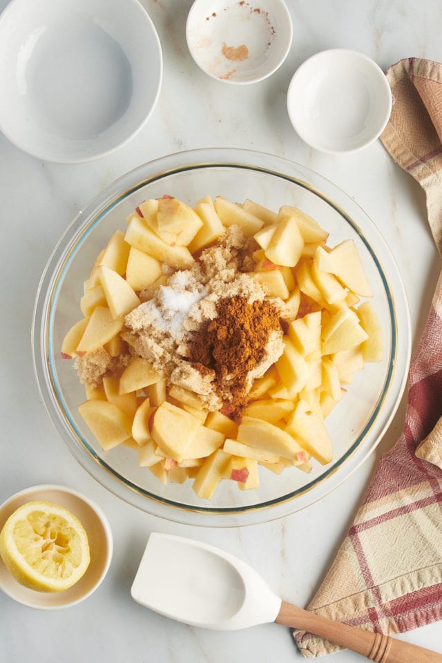 Overhead view of apples in mixing bowl with cinnamon, sugar, and salt