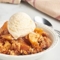 Apple Brown Betty in white bowl with scoop of ice cream on top