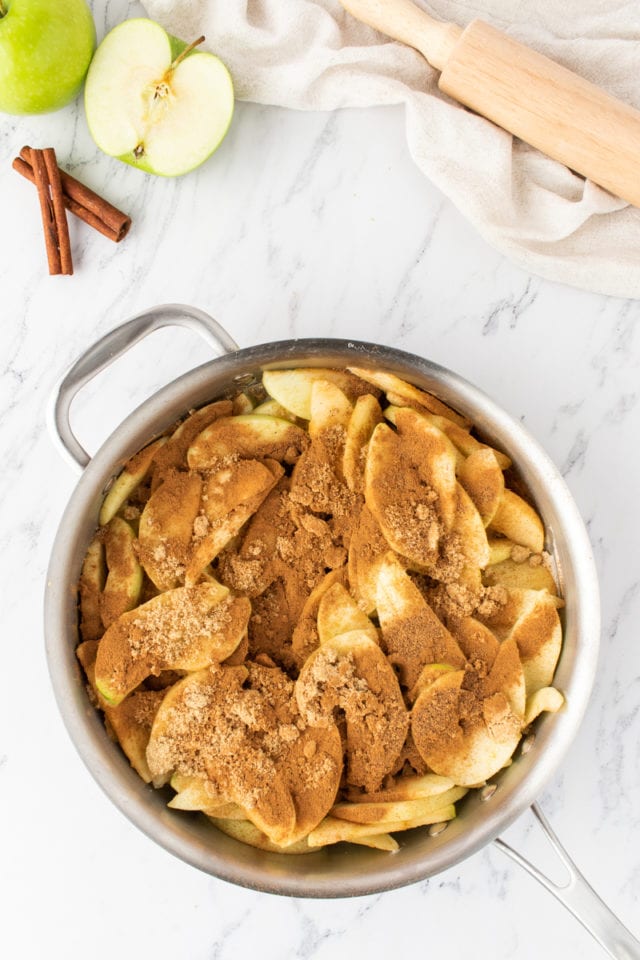 overhead view of sliced apples, brown sugar, cinnamon, and nutmeg in a saucepan