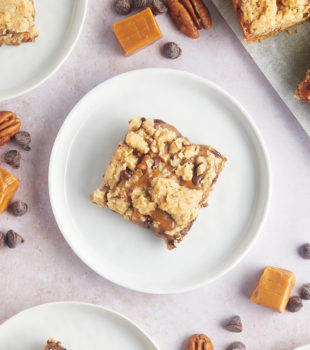 Overhead view of carmelitas on plates with pecans, chocolate chips, and caramels scattered on countertop