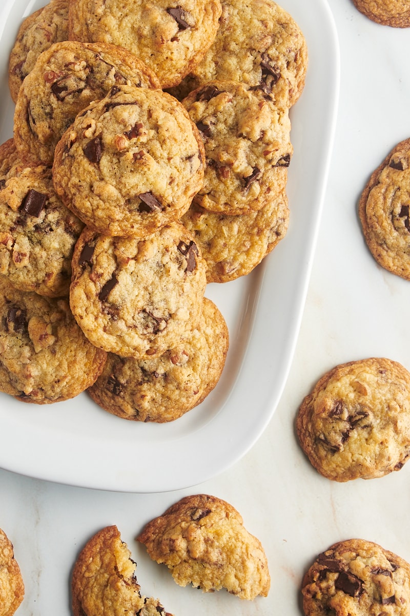 Overhead view of chocolate chunk pecan cookies stacked on platter and on countertop