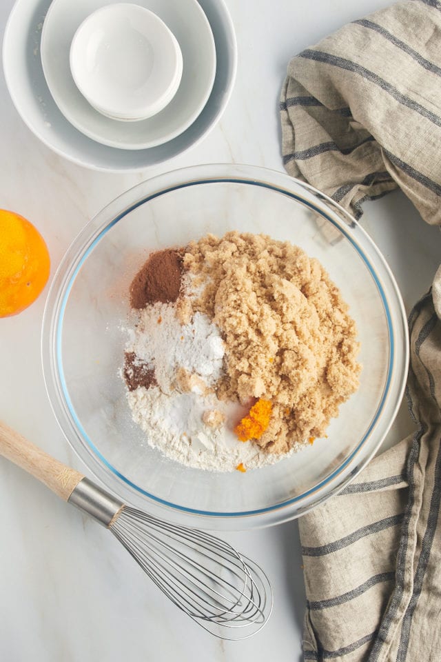 overhead view of flour, brown sugar, baking powder, baking soda, salt, cinnamon, nutmeg, and orange zest in a glass mixing bowl