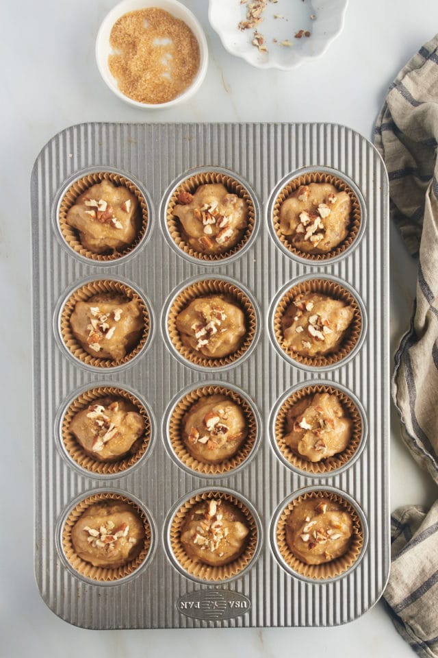 overhead view of portioned date nut muffin batter topped demerara sugar and chopped pecans