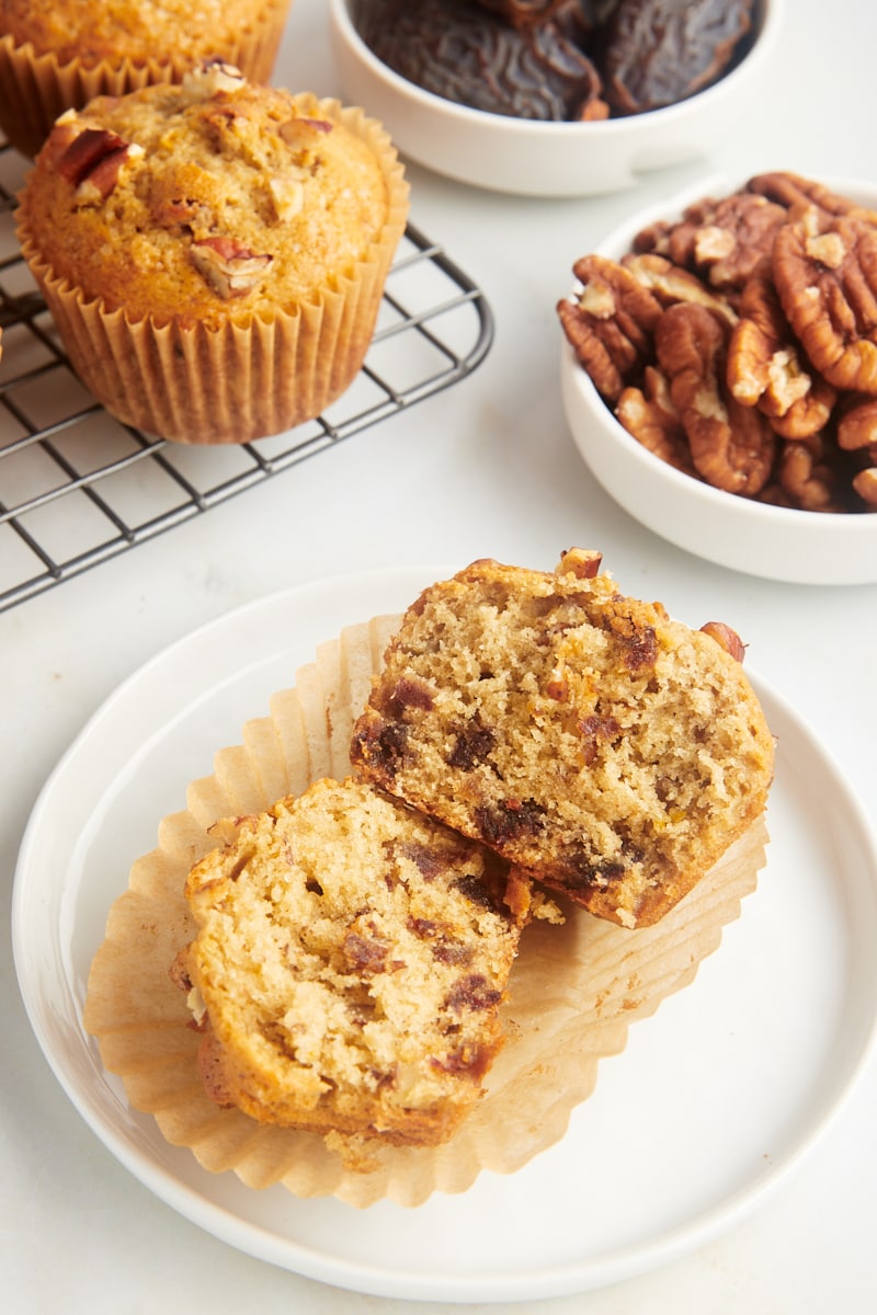 a date nut muffin split in half on a white plate with more muffins in the background