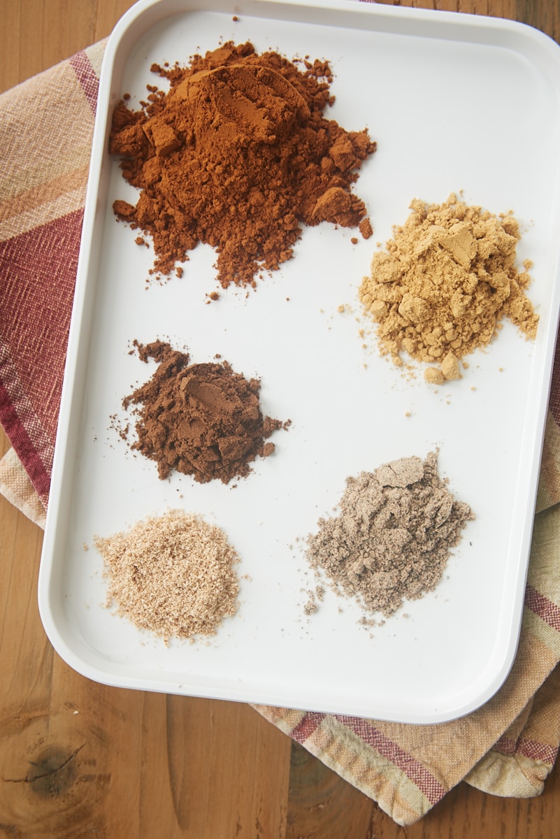 overhead view of cinnamon, nutmeg, ginger, allspice, and cardamom on a small white tray