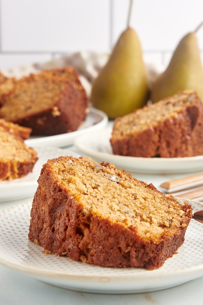Slice of pear bread on plate with additional plates of bread and pears in background