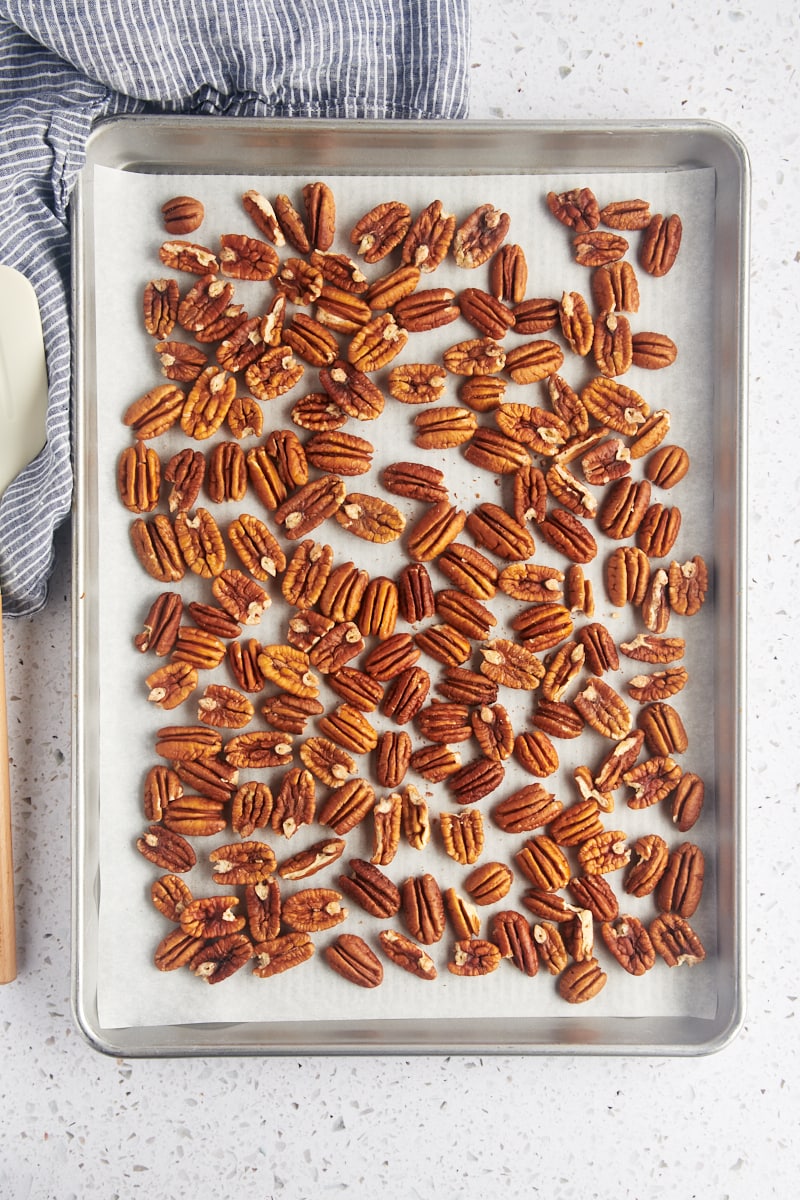 overhead view of pecan halves spread on a parchment-lined baking sheet
