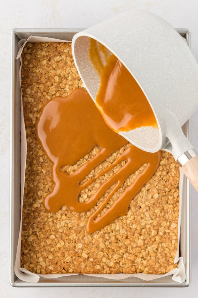 Overhead view of caramel being poured into pan over crust