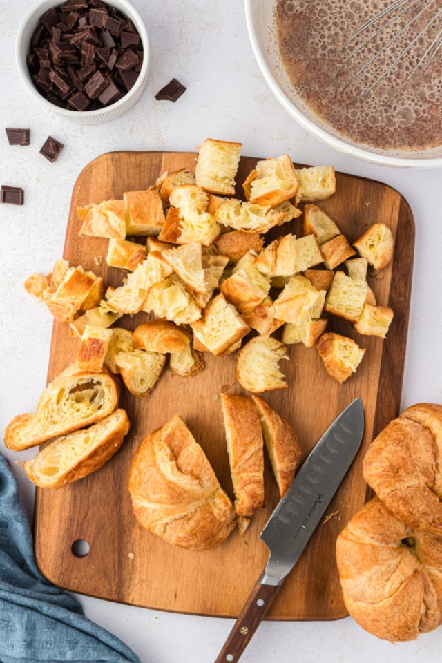 Overhead view of croissants being cut into cubes on cutting board