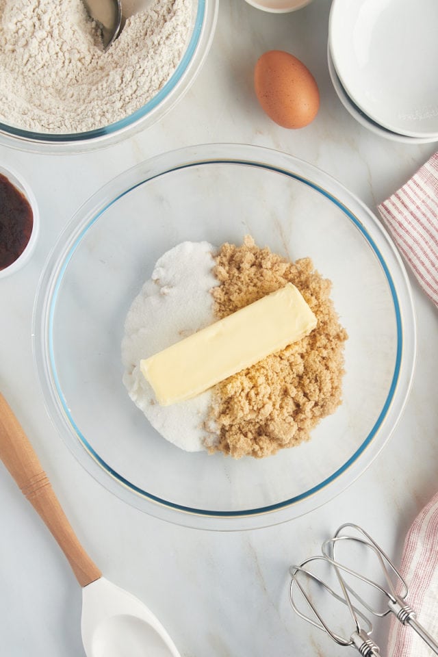 Overhead view of sugar, brown sugar, and butter in a glass mixing bowl.