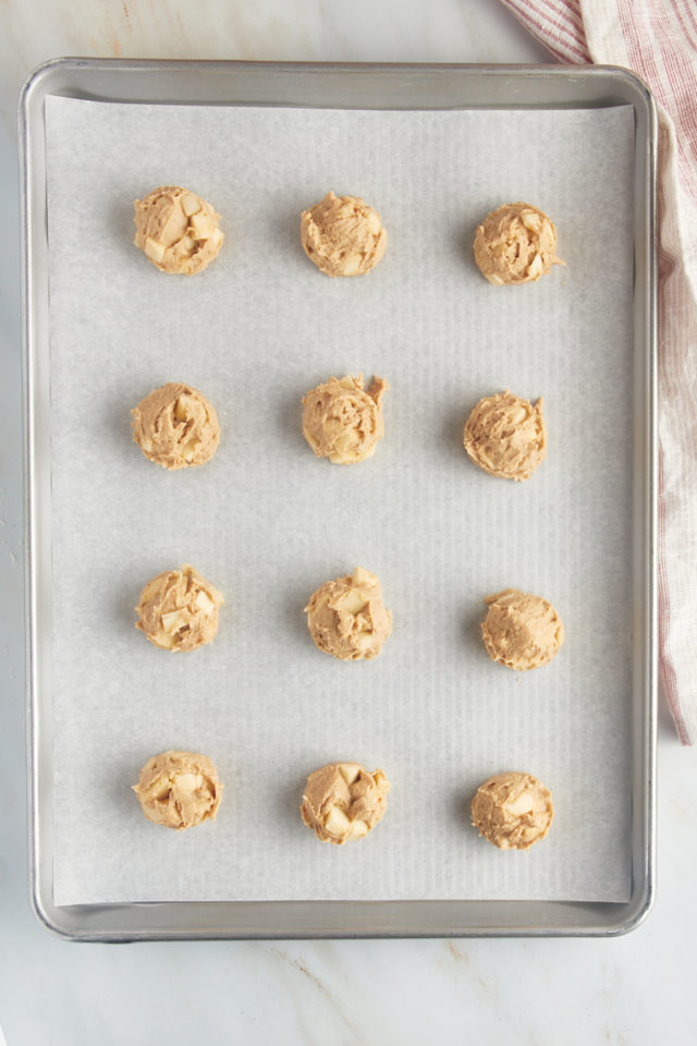 overhead view of portioned apple cookie dough on a parchment-lined baking sheet