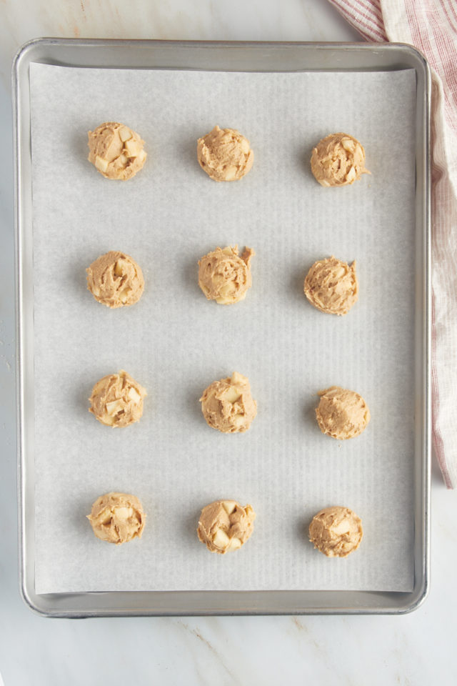 Overhead view of portioned apple cookie dough on a parchment-lined baking sheet.