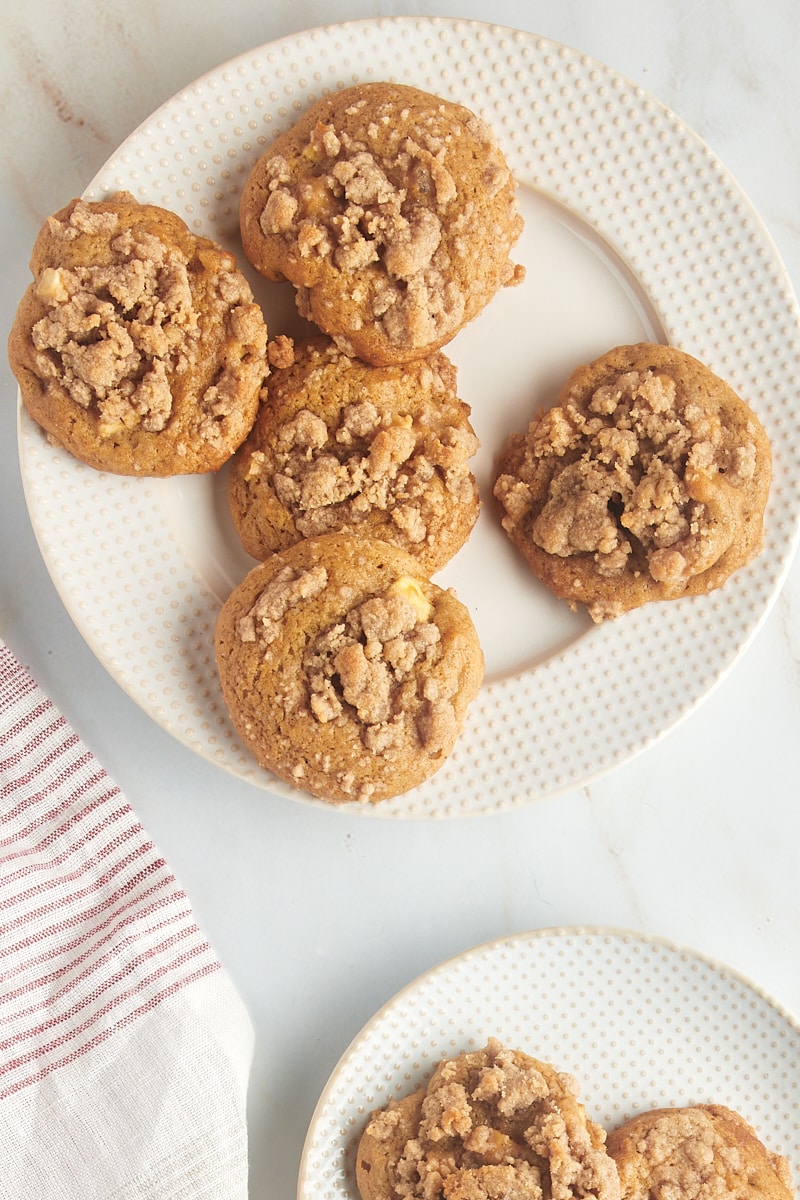 Overhead view of crumb-topped apple cookies on a white and beige plate.