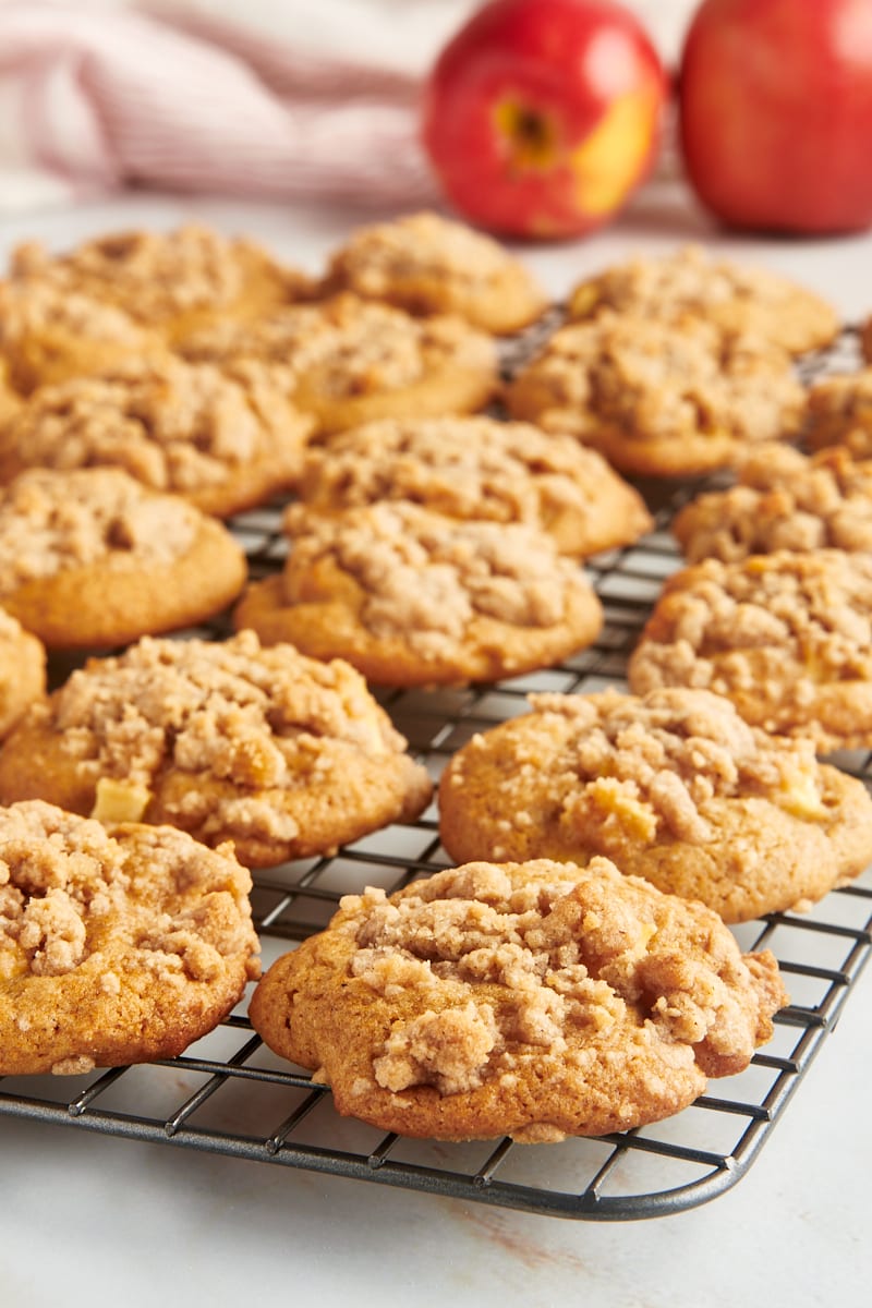 Crumb-topped apple cookies on a wire rack with two apples in the background.