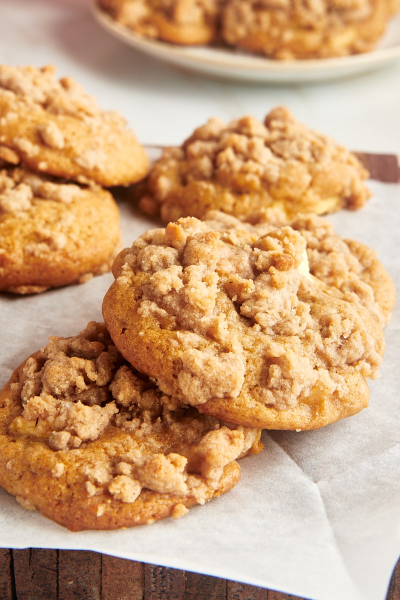 Two overlapping crumb-topped apple cookies on parchment paper with more cookies behind them.