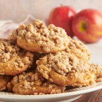 crumb-topped apple cookies piled on a plate with two apples in the background