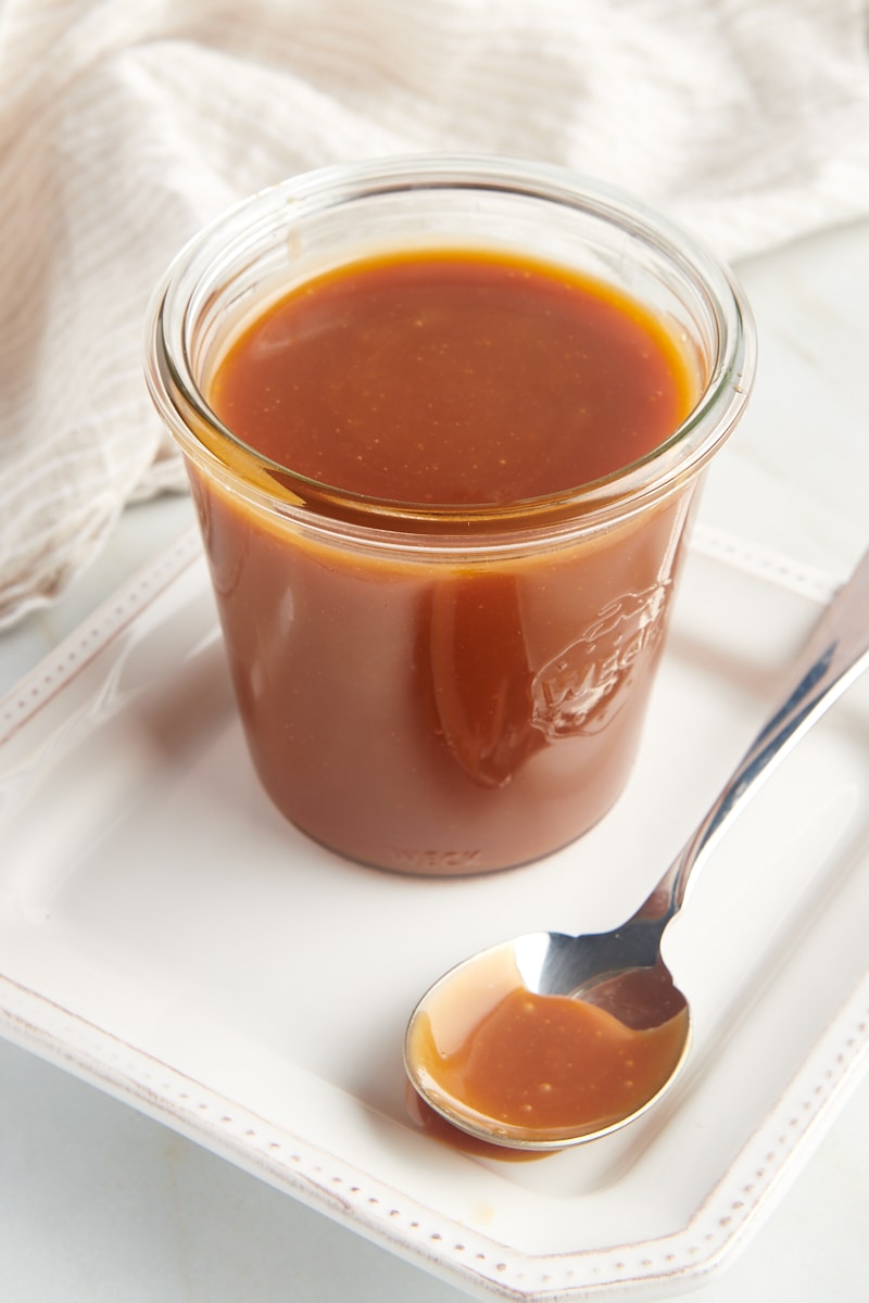 a jar of homemade caramel sauce on a white plate with a spoon next to it