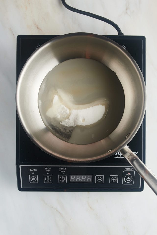 overhead view of sugar, water, and corn syrup in a saucepan on an induction cooktop
