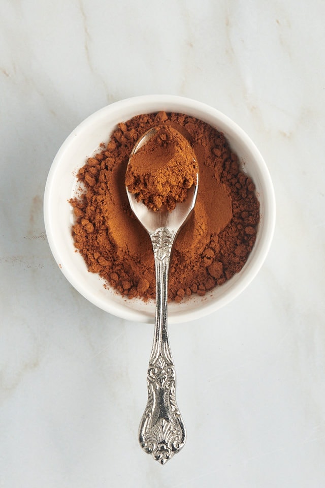 overhead view of a spoonful of cassia cinnamon in a shallow white bowl with more cinnamon in it