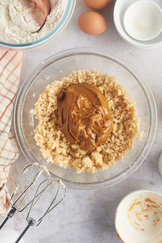 overhead view of cookie butter and vanilla extract added to creamed butter and sugar in a glass mixing bowl