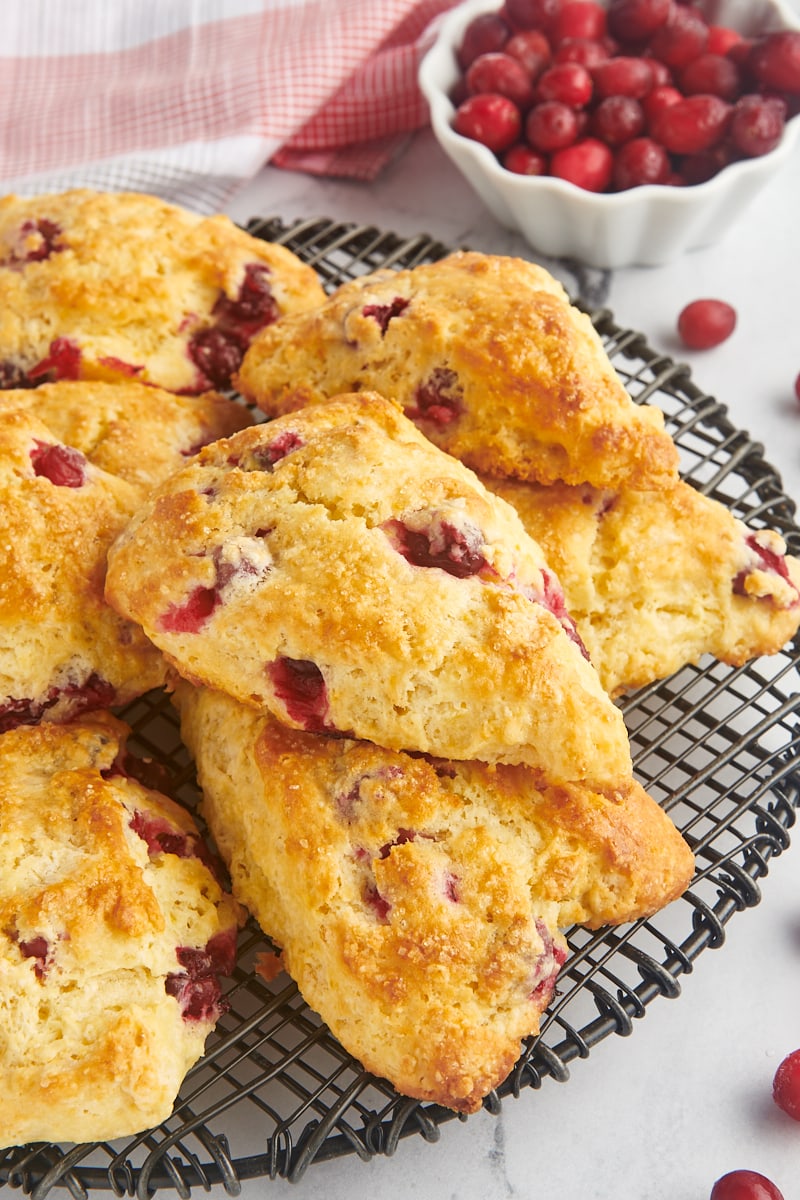 cranberry orange scones piled on a wire rack with a bowl of cranberries in the background