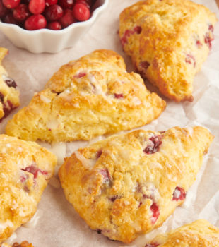 glazed cranberry orange scones on parchment paper alongside a small bowl of cranberries