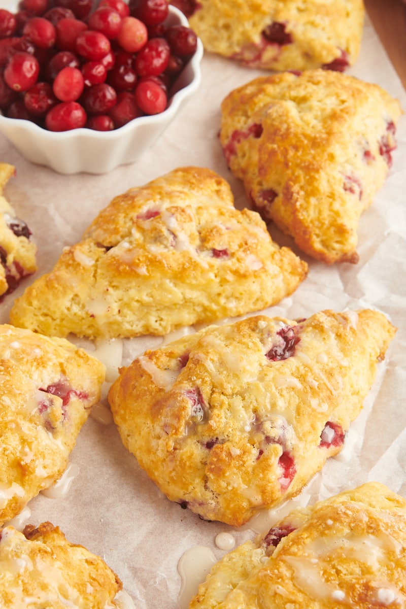 glazed cranberry orange scones on parchment paper alongside a small bowl of cranberries