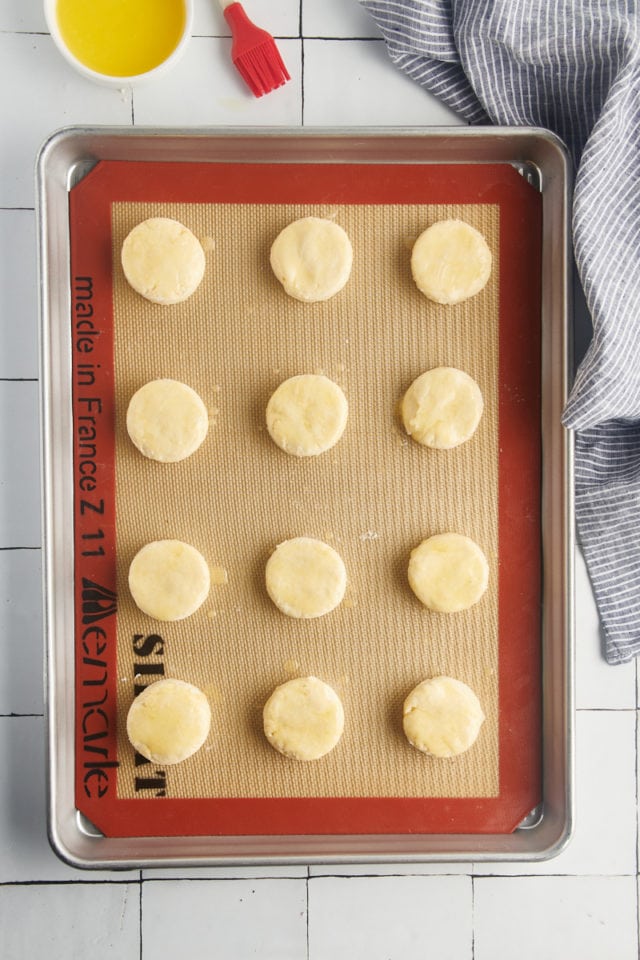 Overhead view of unbaked cream biscuits on silpat lined baking sheet after brushing with butter