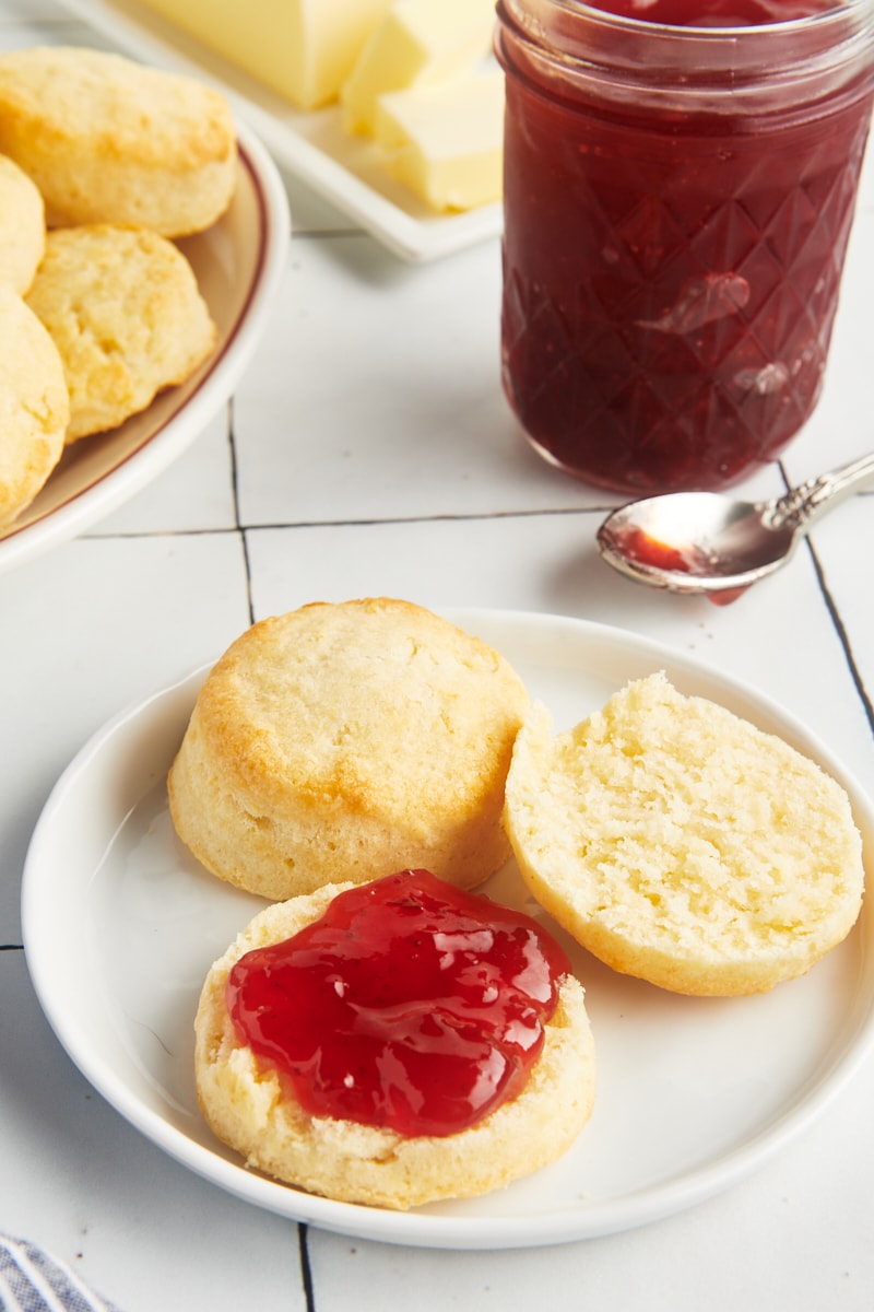 Two biscuits on plate with one sliced and covered with jam