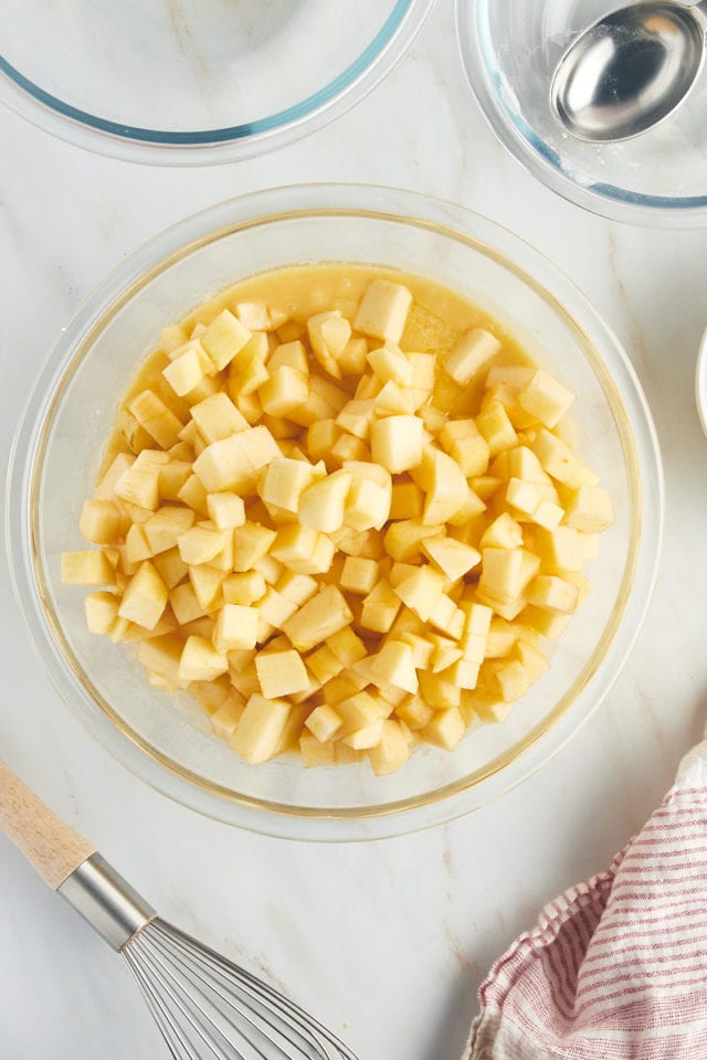 overhead view of apples added to cake batter in a glass mixing bowl