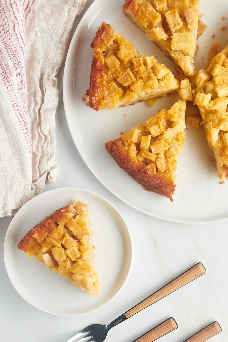 overhead view of a slice of French apple cake on a white plate with the remaining cake on a white cake plate