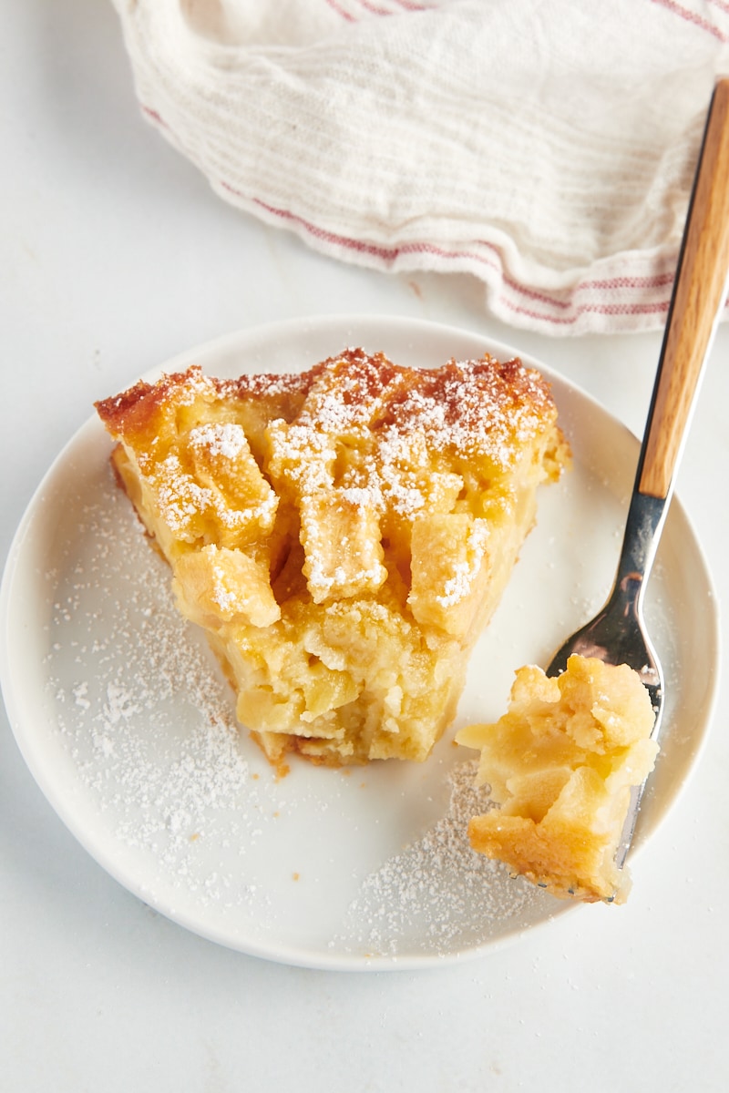 a slice of French apple cake on a white plate with a bite of cake on a fork
