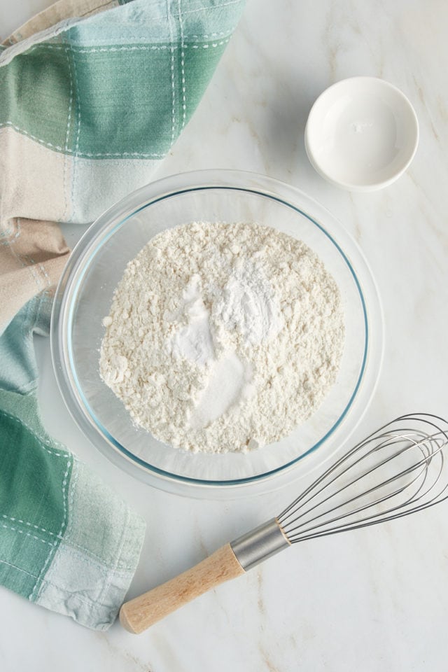 overhead view of cake flour, baking powder, baking soda, and salt in a glass mixing bowl