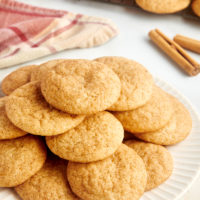 Pile of snickerdoodles on white plate with wire rack of cookies in background