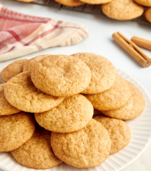 Pile of snickerdoodles on white plate with wire rack of cookies in background