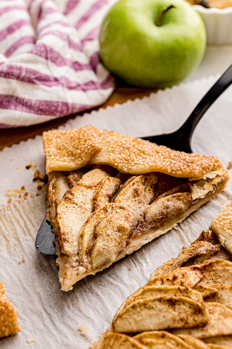 a slice of apple galette on a pie server set on parchment paper