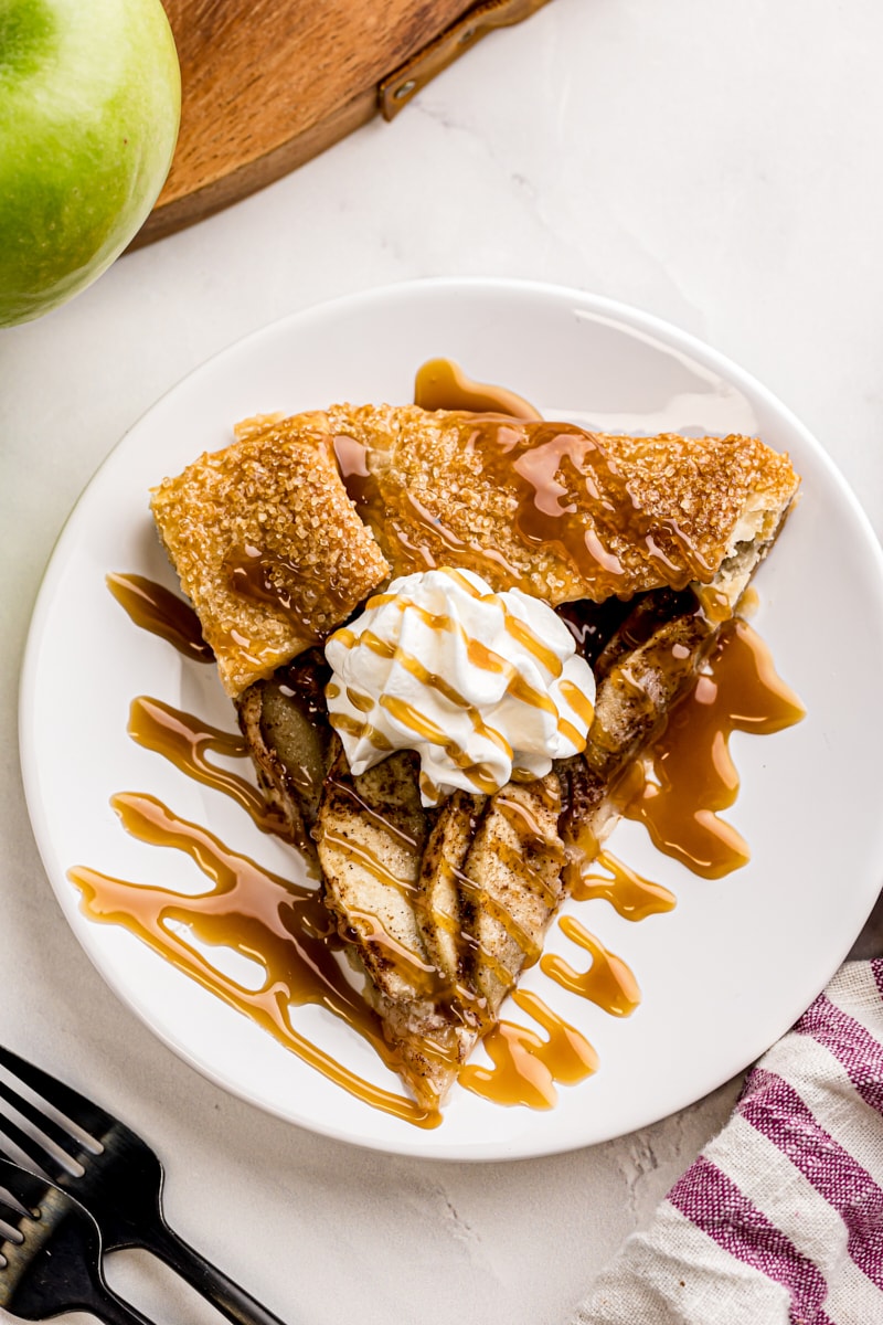 overhead view of a slice of apple galette topped with whipped cream and caramel sauce