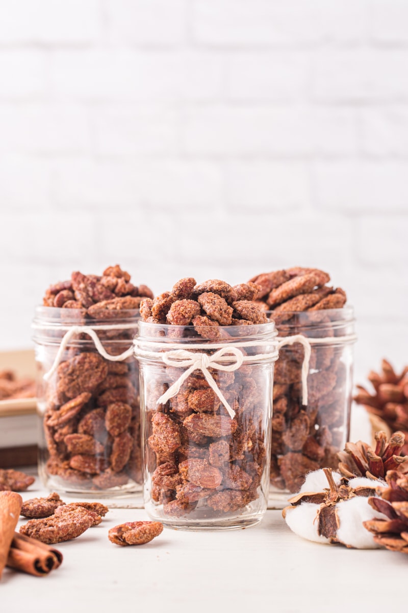 three mason jars filled with candied nuts and tied with a white ribbon